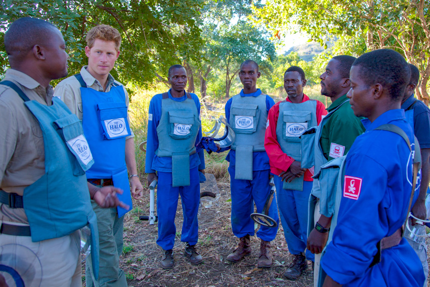 Prince Harry stands and talks with a HALO demining team in Angola whilst wearing PPE