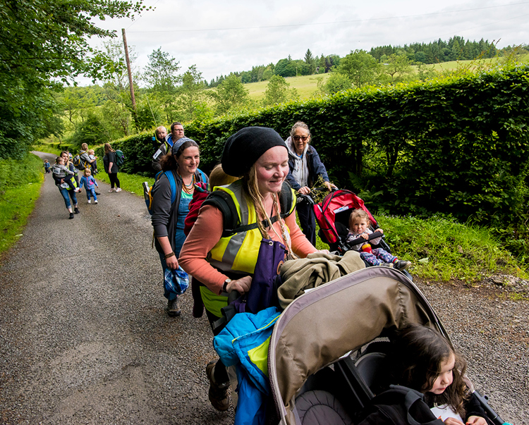 Adults push buggies down a country path as they walk for Syria