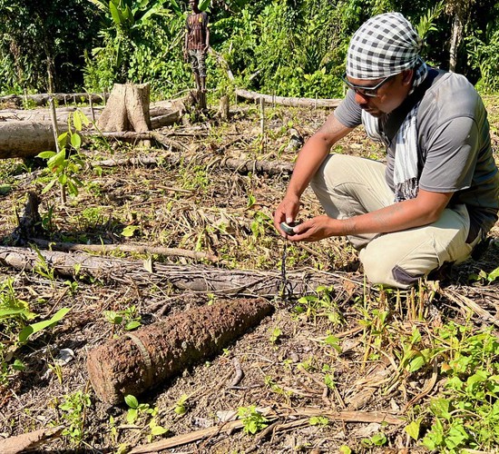 Stephen Talu, HALO's programme manager, crouches towards the ground holding a device