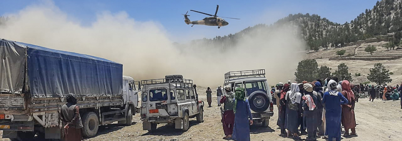 Helicopter flies over vehicles and people in rural Afghanistan