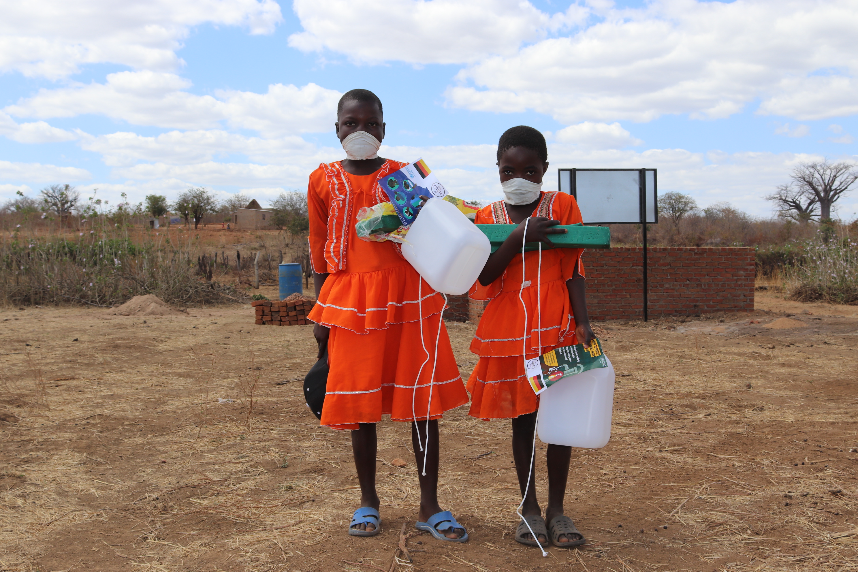 Two Zambian children in a rural area holding bottles and Covid-19 leaflets