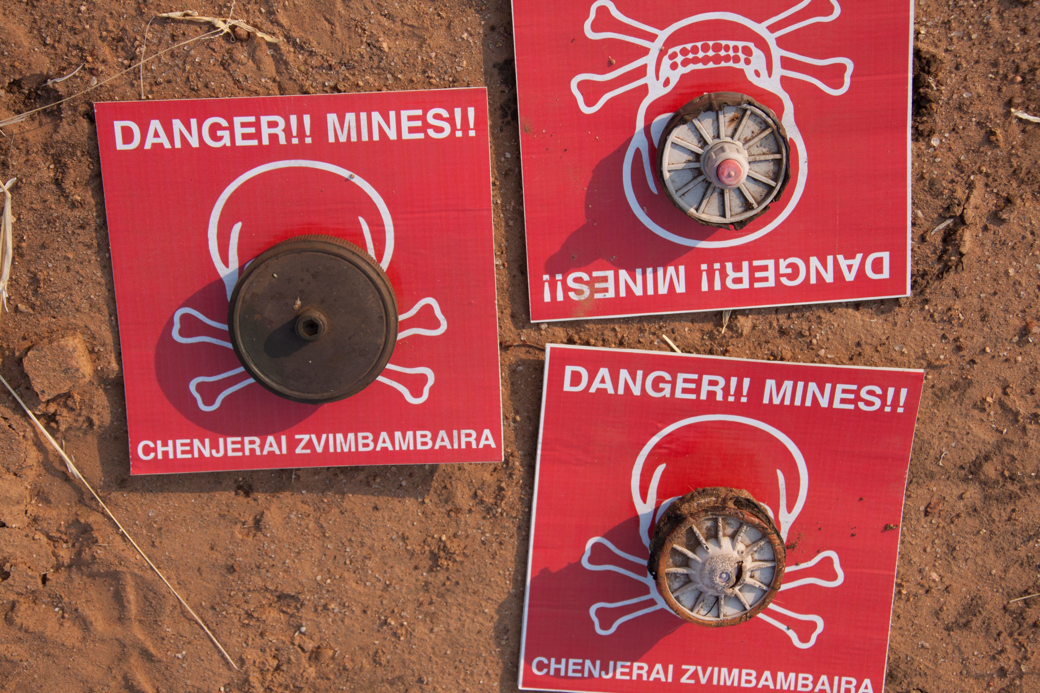 Mine warning signs lay on the soil with mines on top of them