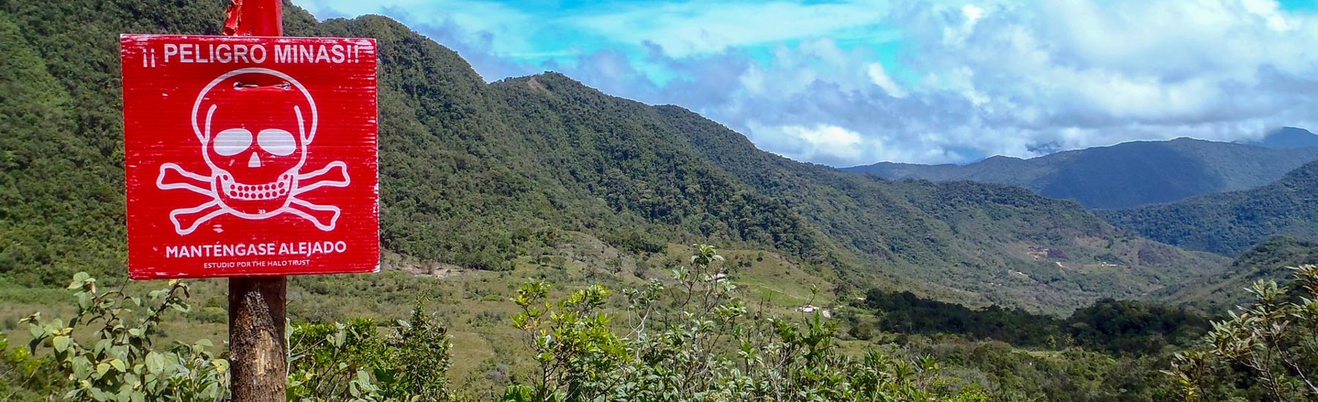 A red mine warning sign stands alone with a vast view of mountainous terrain in the background