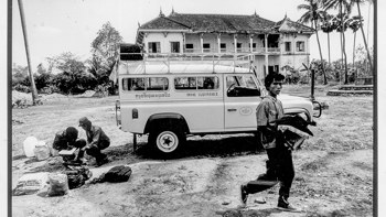 A black and white image of a HALO vehicle in front of a house in Cambodia, with HALO Trust staff 