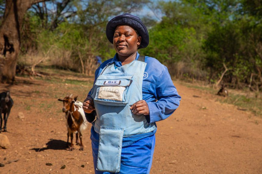 Faith, a deminer paramedic from Zimbabwe stands in HALO uniform and PPE on a sandy track