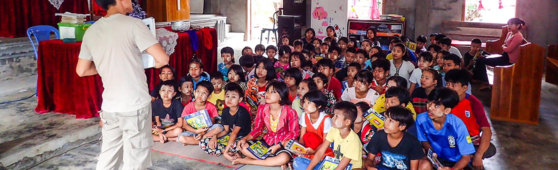 Children sitting on the floor receive a mine risk education session from a HALO instructor.