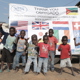 A large group of children smile and give a thumbs-up to the camera in front of a banner declaring Mozambique's mine free status