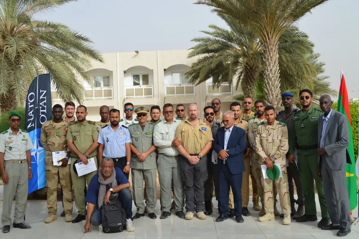 A posed group shot of the HALO charity team and the Mauritanian government, with a NATO flag and Mauritania flag in the background