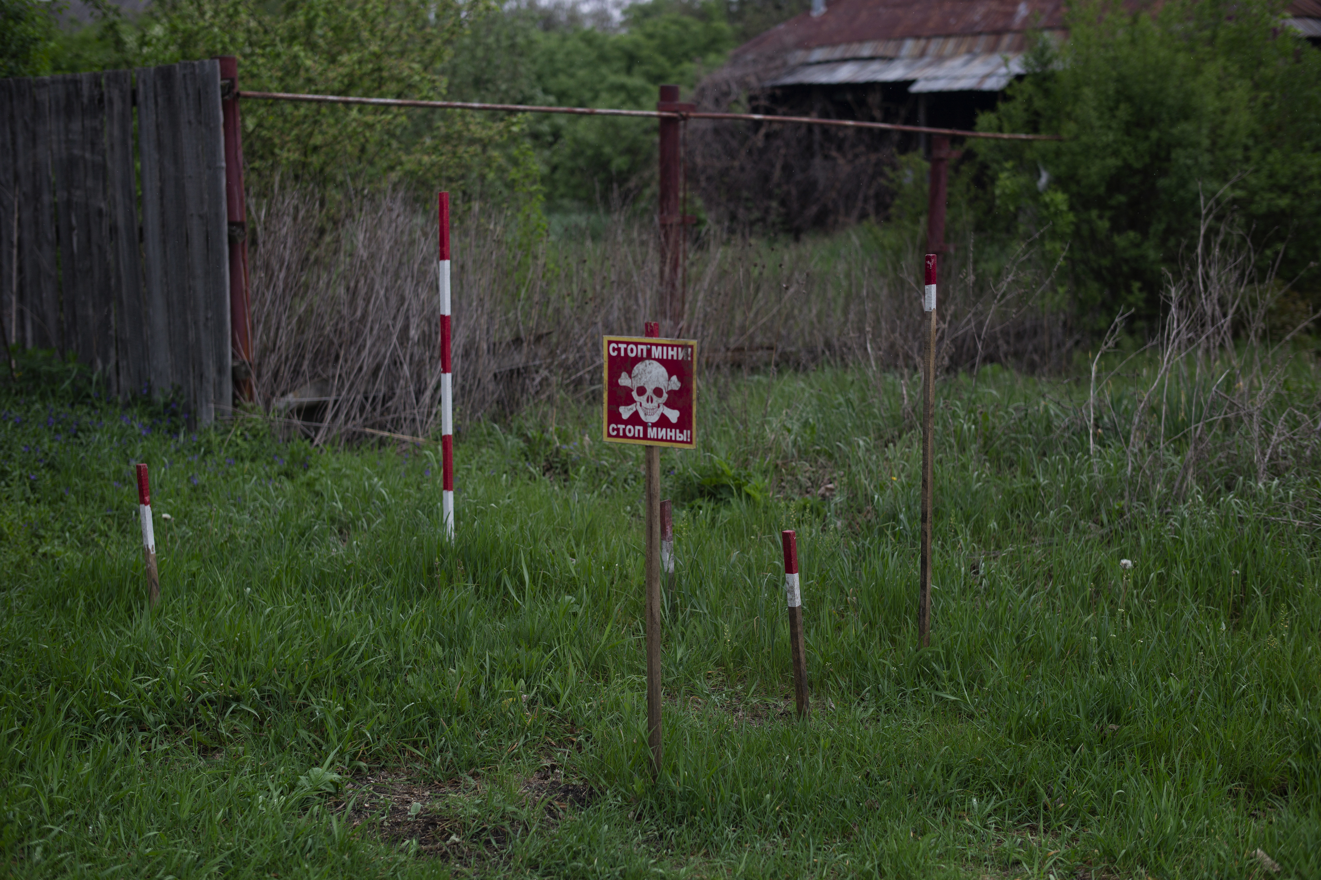 Mine markers and a warning sign are planted in the grass