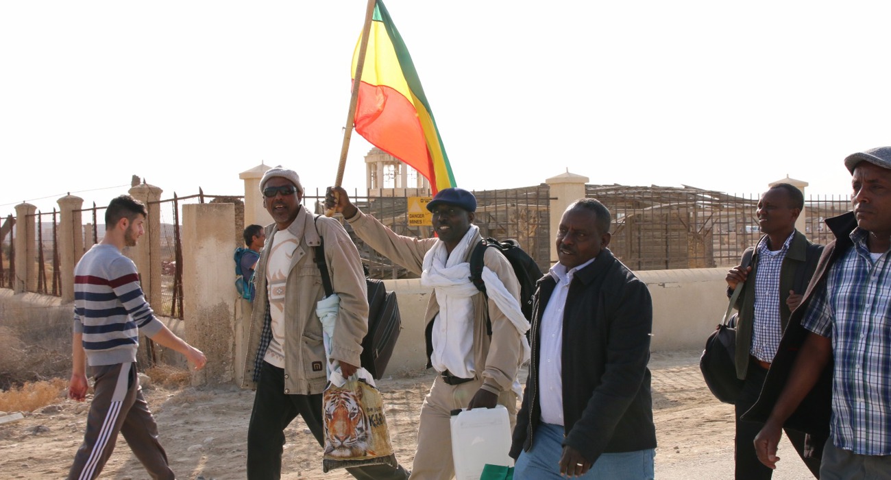 Pilgrims walk through the Baptism Site waving a flag