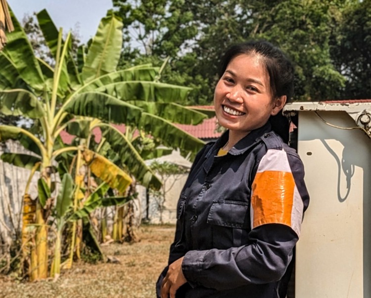 Natmany Inthisone, Team Leader in Laos stands in front of buildings and palm trees