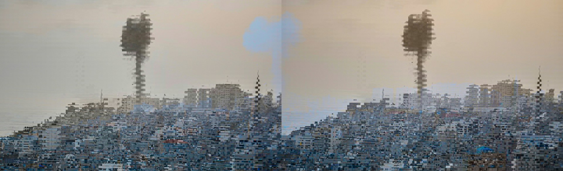 An aerial view of the damaged city of Gaza with a plume of smoke from an explosion rising in the distance