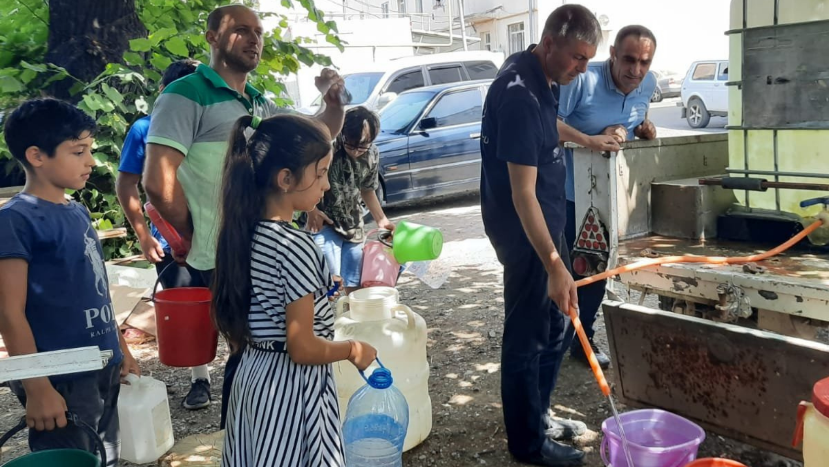 Children and adults stand around an outdoor tap to fill up containers with water