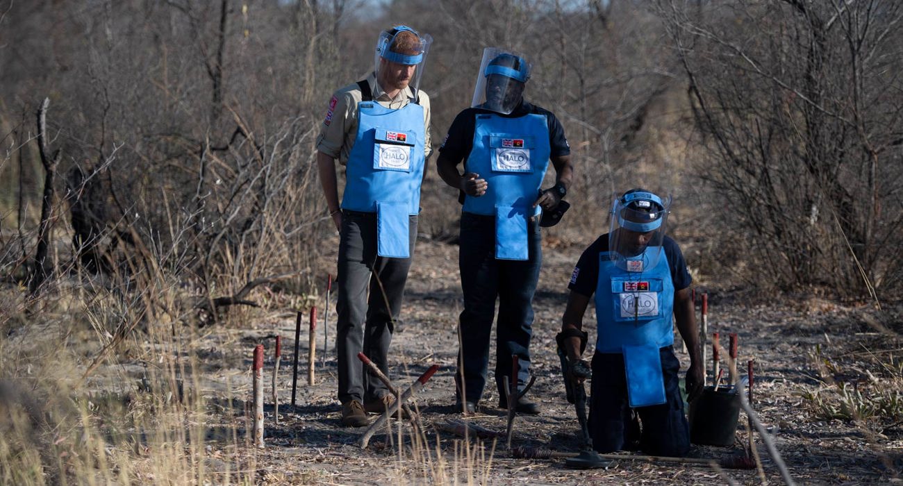 Prince Harry watches a demonstration by HALO Trust deminers whilst wearing PPE