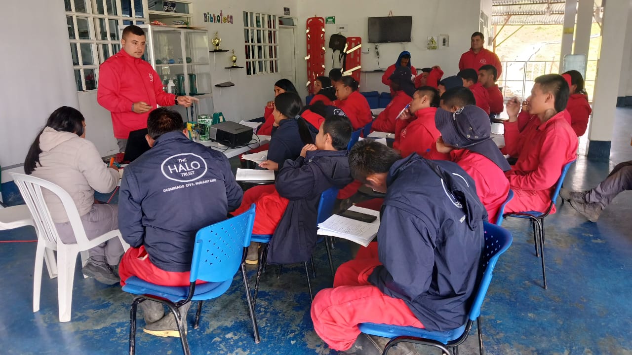 Standing before a HALO team in a classroom, John Alexander leads the group in a training session.
