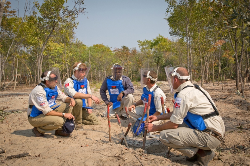 Prince Harry kneels with a team of HALO deminers in a rural minefield in Angola