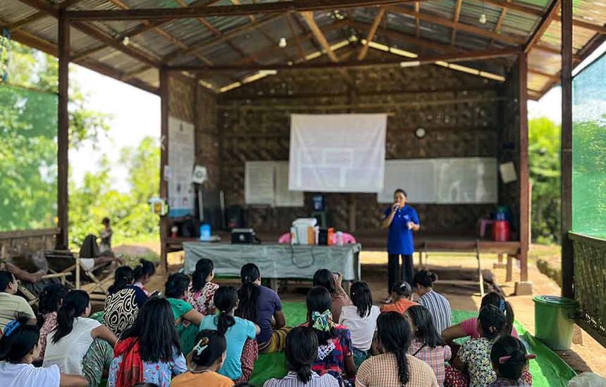 Women sitting on the floor of a tarpaulin-roofed classroom receive risk education sessions in Myanmar.