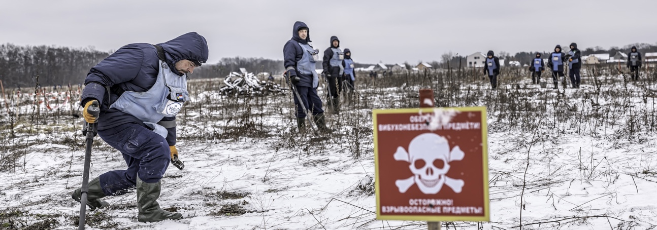 A red danger mines sign in front of HALO Trust staff working to clear landmines in a snow covered minefield in Ukraine