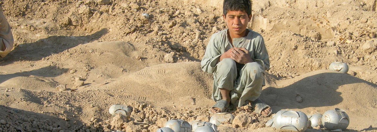 Boy squatting next to cluster munitions in Afghanistan