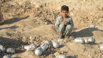 Boy squatting next to cluster munitions in Afghanistan