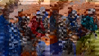 Group of Somaliland men sitting on burnt orange earth playing a game with date stones