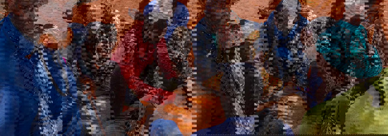 Group of Somaliland men sitting on burnt orange earth playing a game with date stones