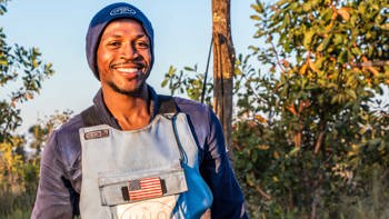 A male deminer wearing HALO uniform with a USA badge smiles