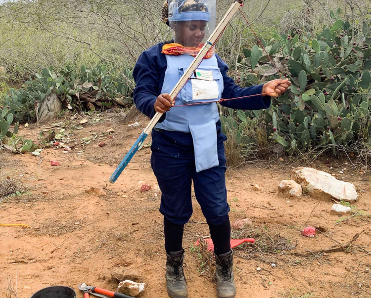 Albertina, a deminer in Angola, holds a stick and piece of string while wearing PPE