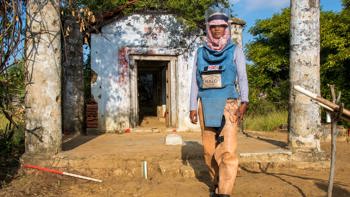 A woman wearing PPE stands in front of an old building with pillars