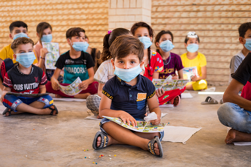 Children sit on the floor reading risk education materials wearing face masks