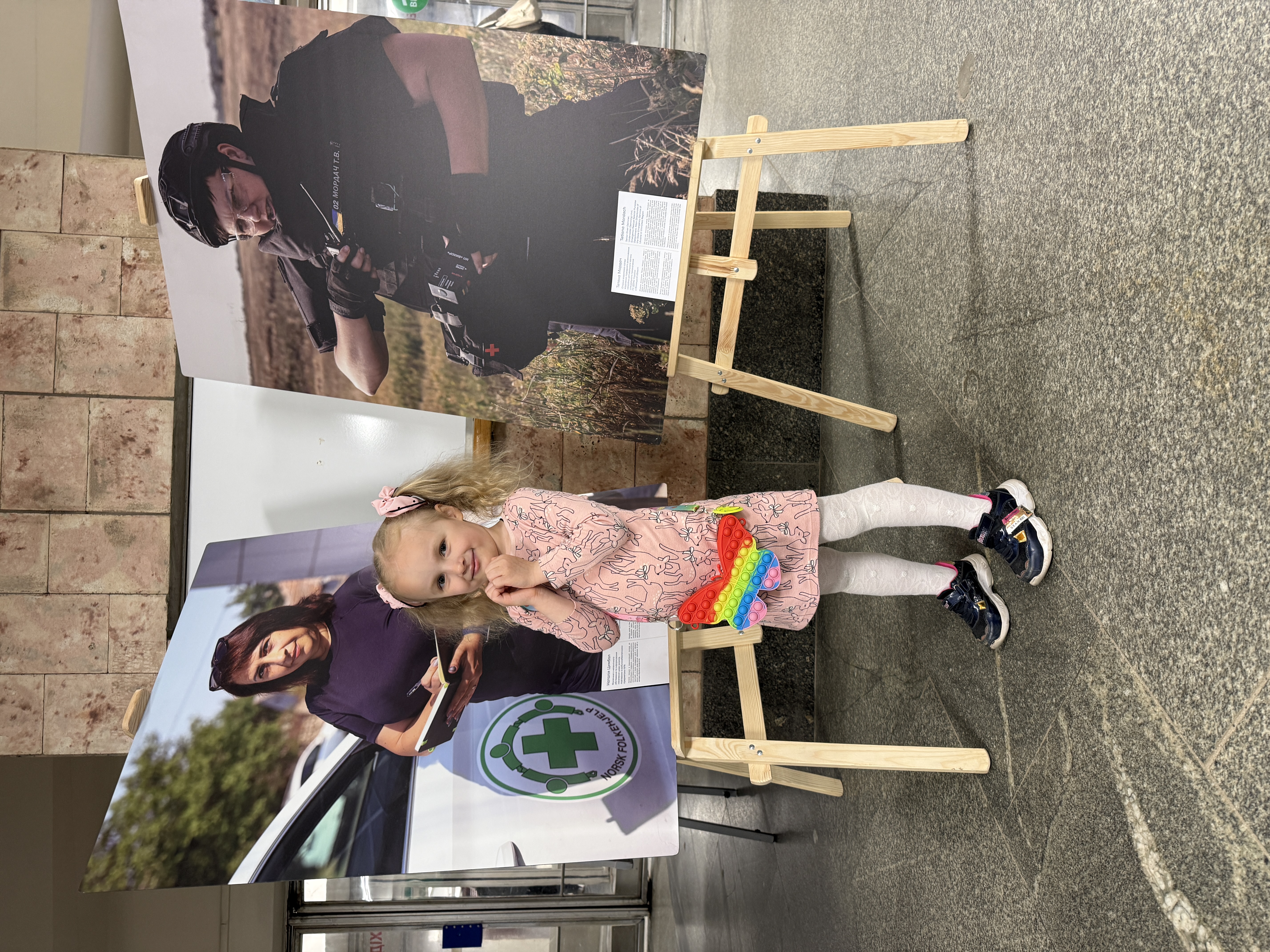 Malenka divchynka fotohrafuietsia na foni portretiv heroin vystavky
