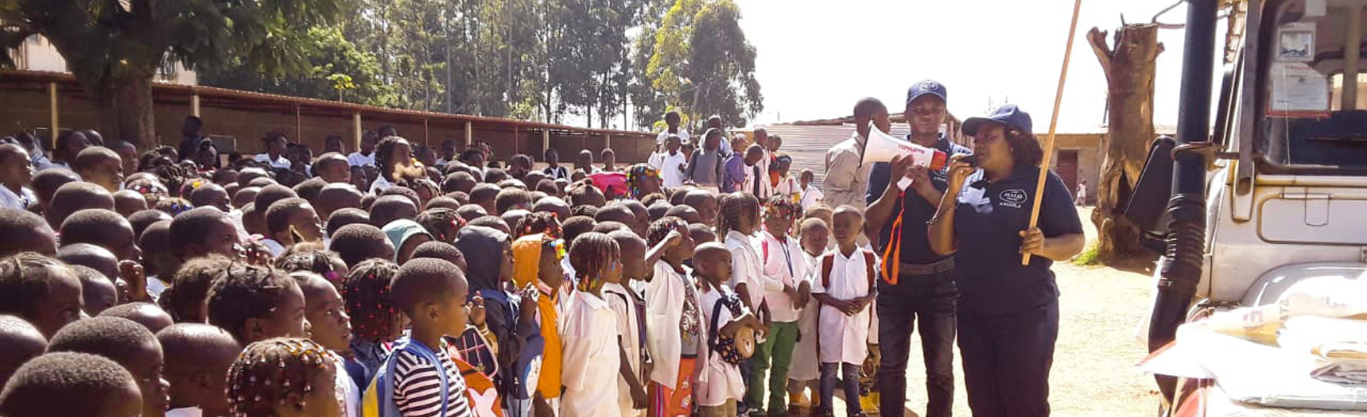 A large group of kids stand in line as they look up to a HALO staff member speaking with a megaphone outside