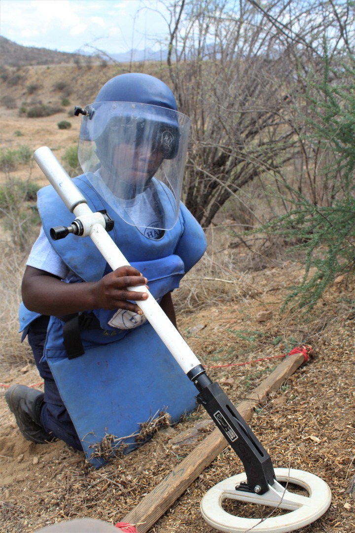 A HALO deminer kneels with a metal detector in Angola
