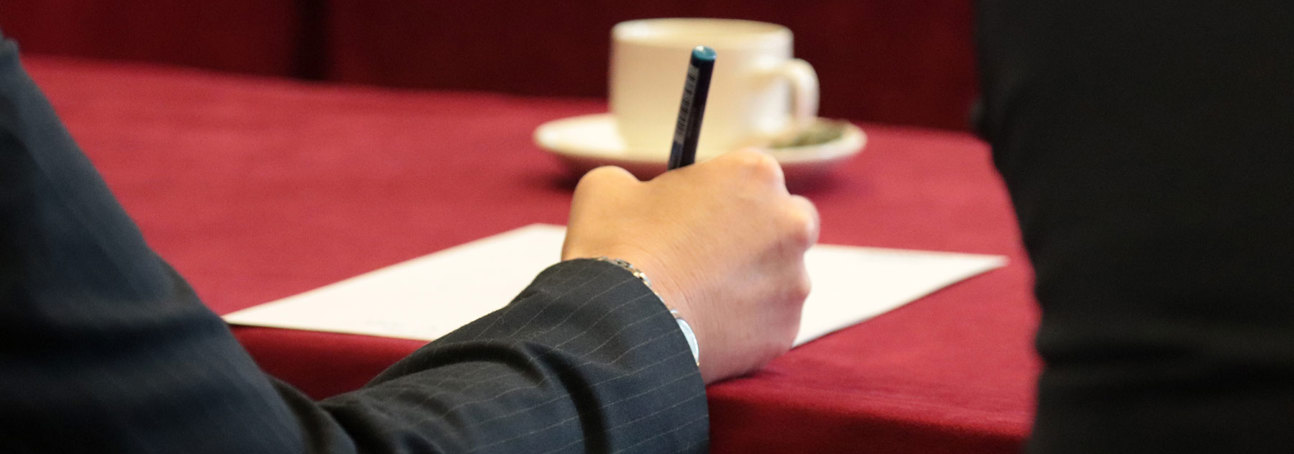 A hand holding a pen to take notes at an event at Chatham House