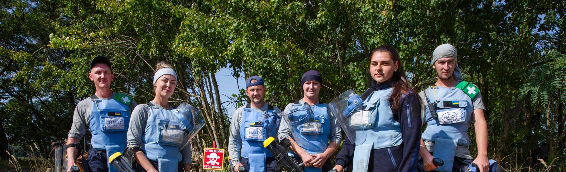 Demining team in Chernihiv, pose next to a mine warning sign with their metal detectors