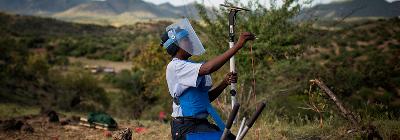 Joanna, a HALO Trust deminer, carefully kneels whilst using a detector on a rural minefield in Angola