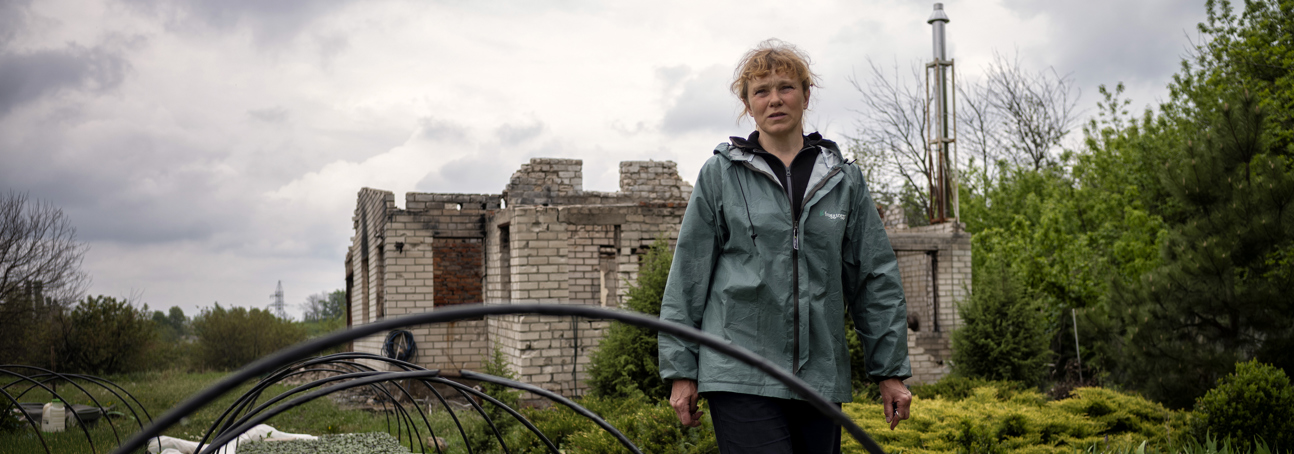 Наталя крокує фермою на фоні зруйнованого будинку