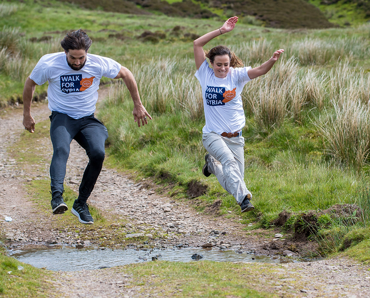 Two people jump over a puddle during their walk for Syria