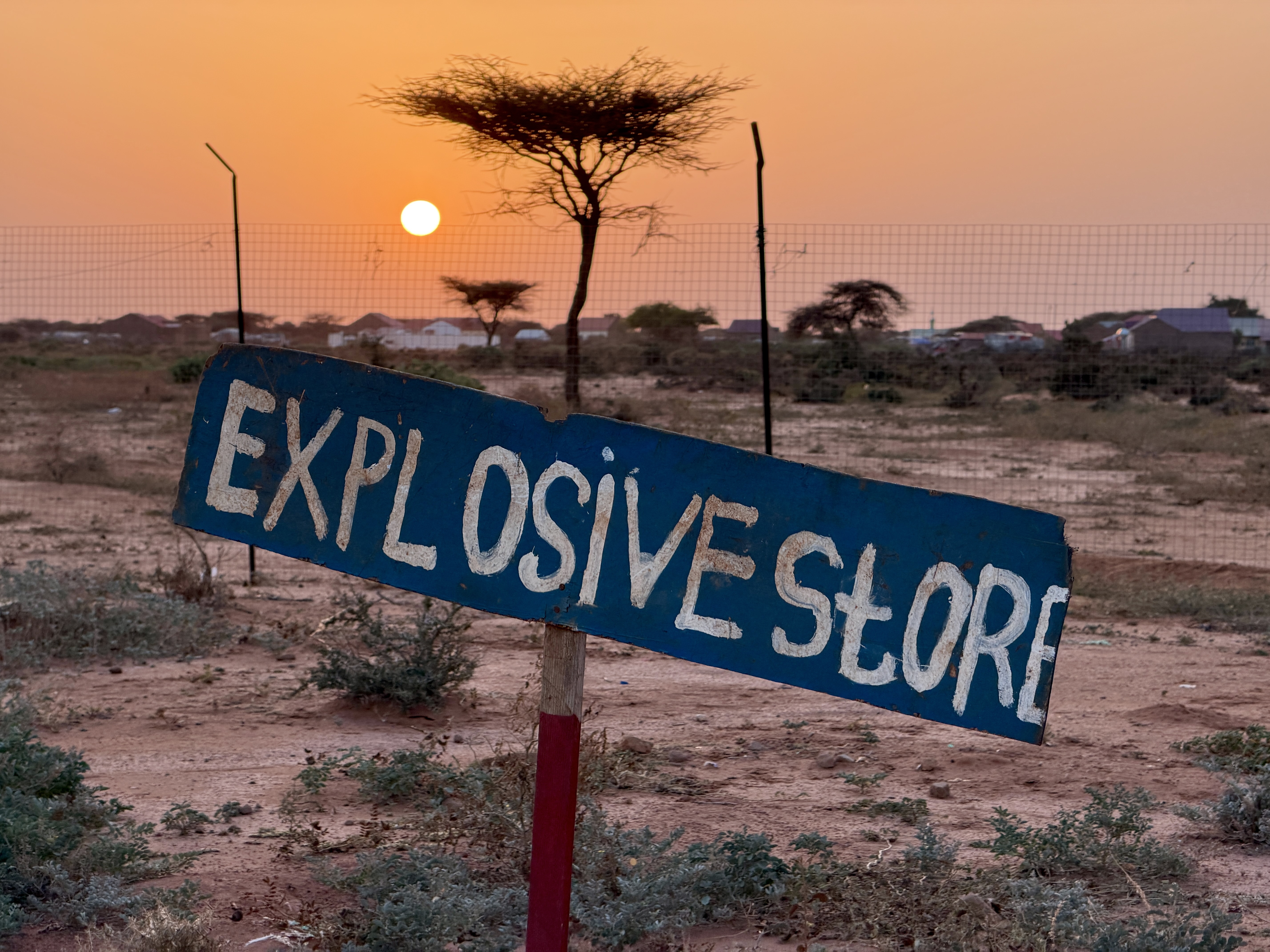 A hand painted sign in the ground in Somalia which reads "Explosive store"