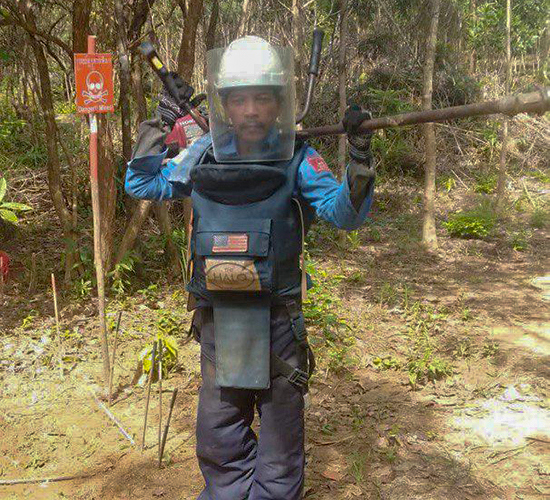 Mr Monn Seit, HALO Cambodia's longest serving deminer wearing PPE and holding a detector in a minefield