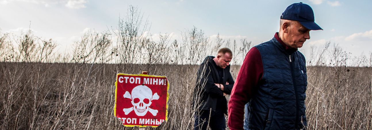Two men walk through a field past a red danger sign in Ukraine