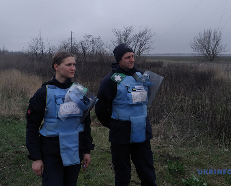 HALO deminers wearing PPE stand in a field as it is getting dark