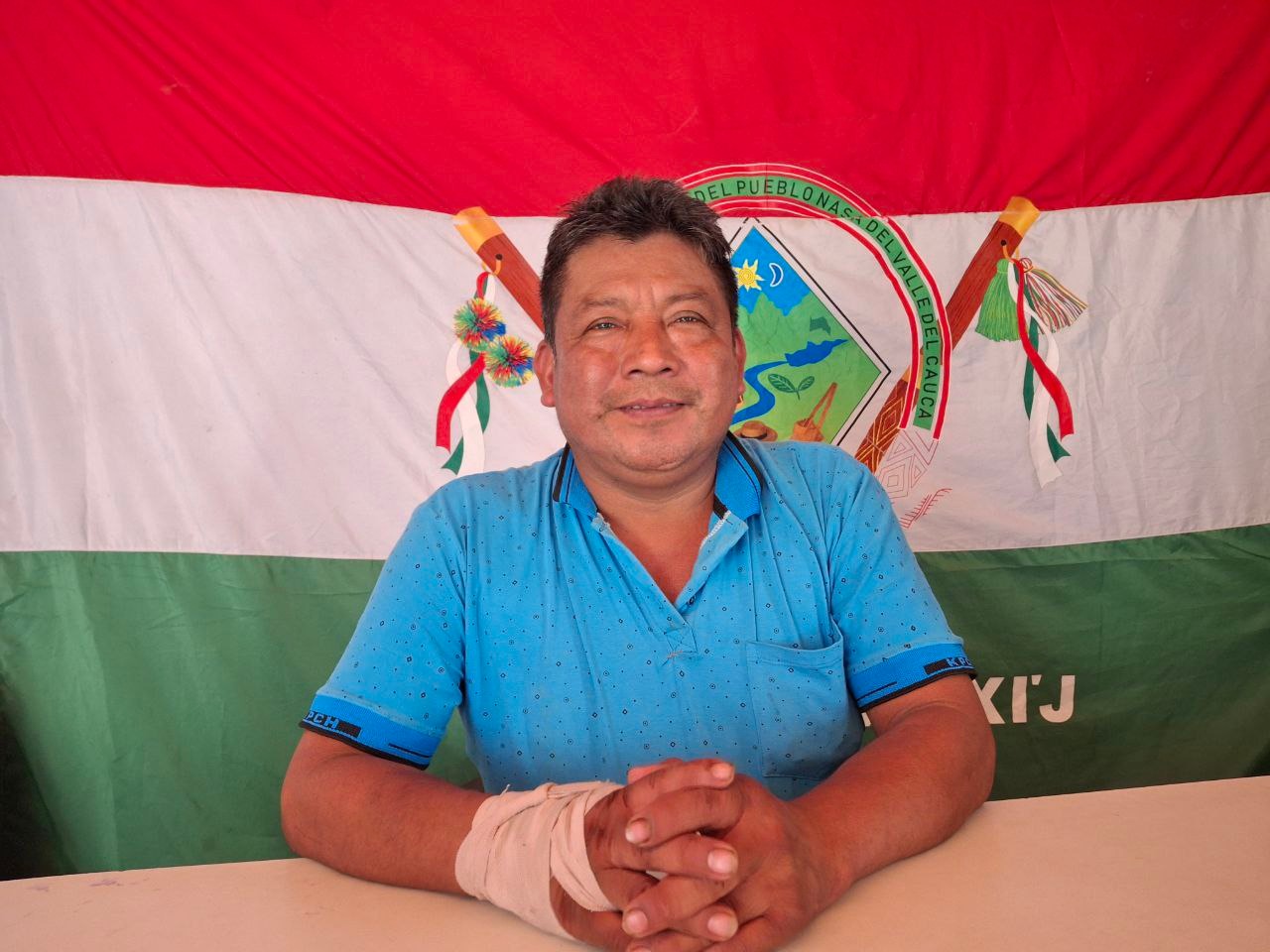 A middle-aged man sits in front of a Valle del Cauca flag 