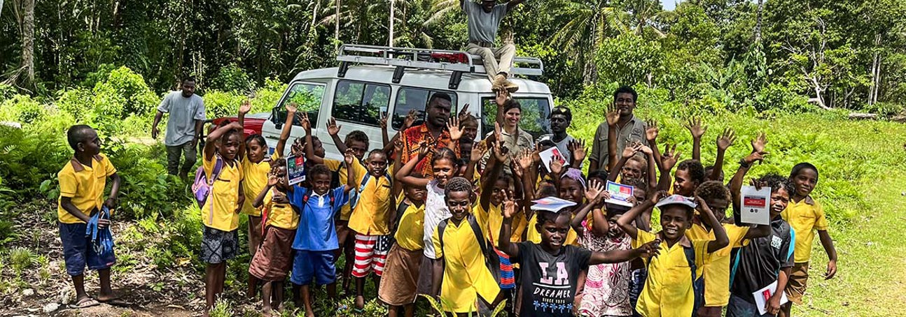A group of kids and HALO staff stand around a vehicle raising their hands in celebration