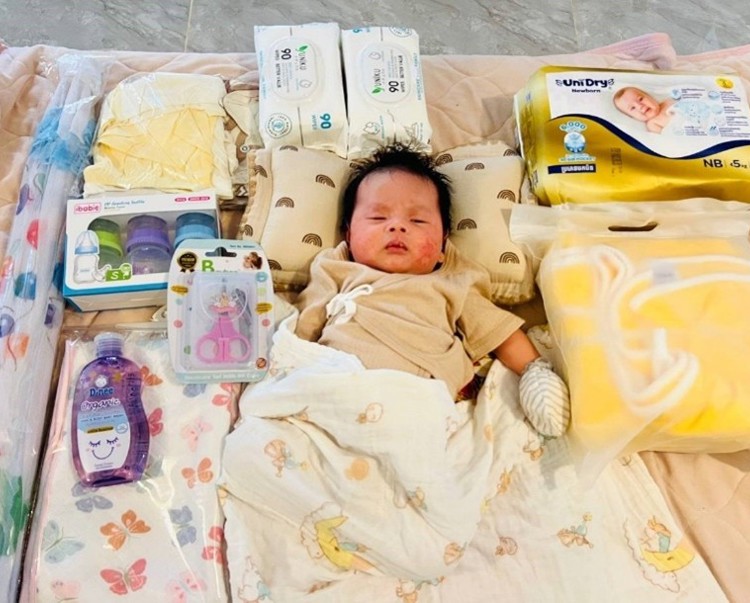 A baby lays on a soft mat with a blanket and maternal care items around them