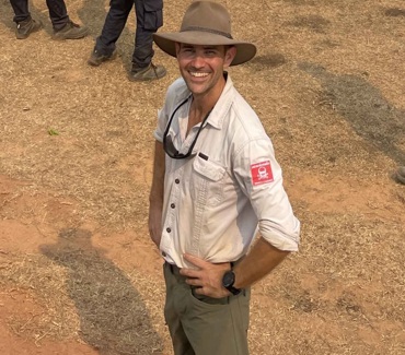 Man smiling and wearing a hat while standing in a field