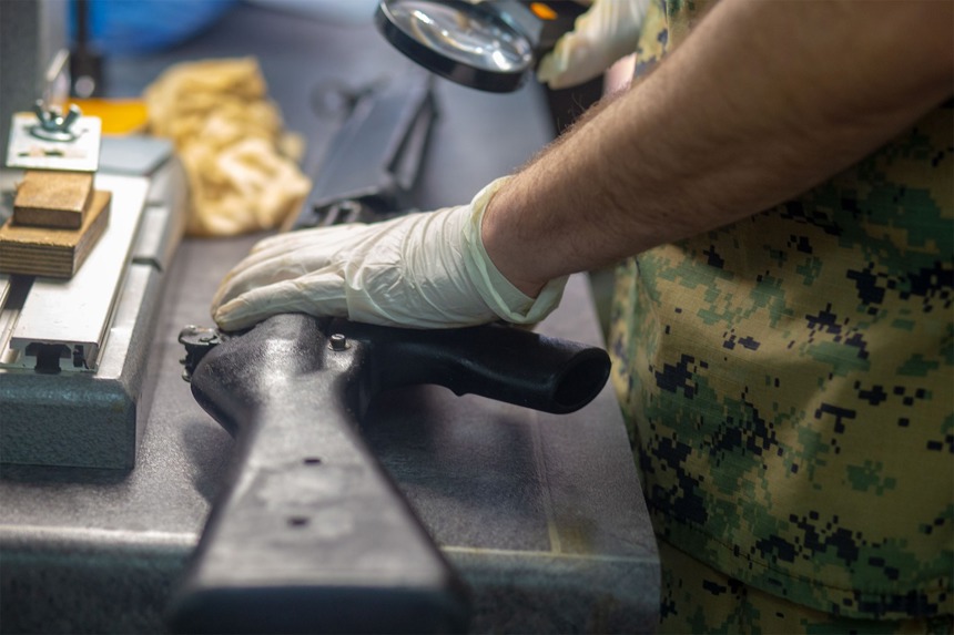 A man wearing gloves inspects a gun with a magnifying glass