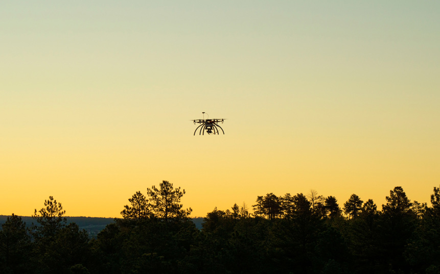 A drone flying over the treeline during sunset