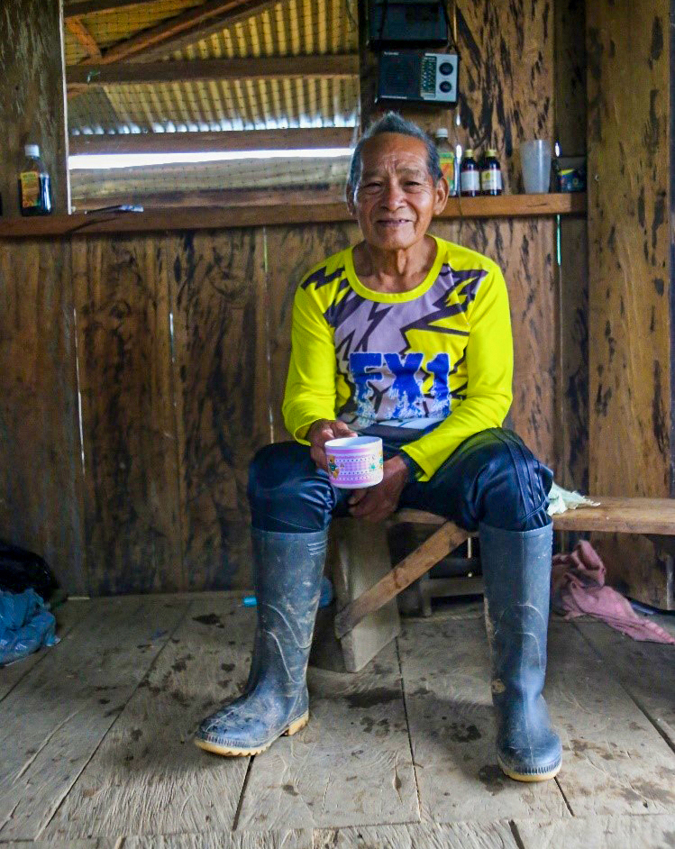 Don Lauro sits on a bench wearing wellies and holding a tea cup