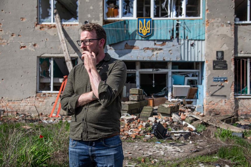 JJ Chalmers standing in front of a bombed house in Hrakove Village, Ukraine